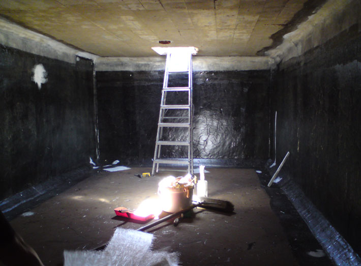 Inside the rectangular concrete water storage tank, fibreglass repairs are made to cracked areas.